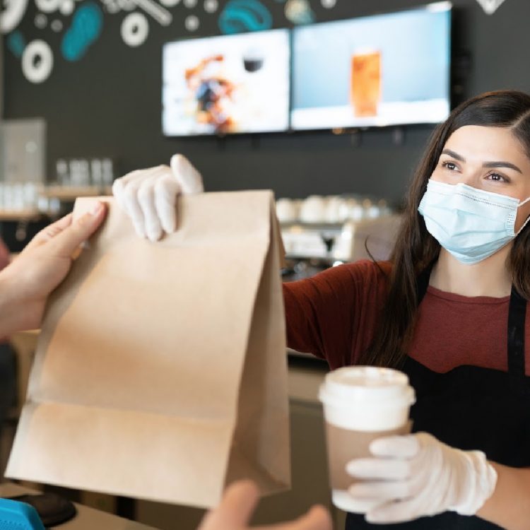 Young female staff giving parcel and coffee to customer at takeaway counter in coffee shop