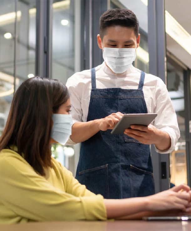 Waiter wear protective face mask taking order from Asian Woman client with digital tablet in modern cafe or restaurant. People in public with new normal life and Lifestyle